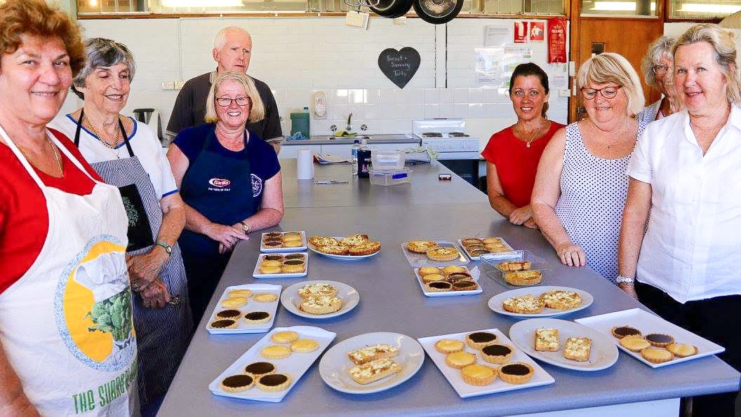 A class of adults gathered proudly around the sweet and savoury tarts they made