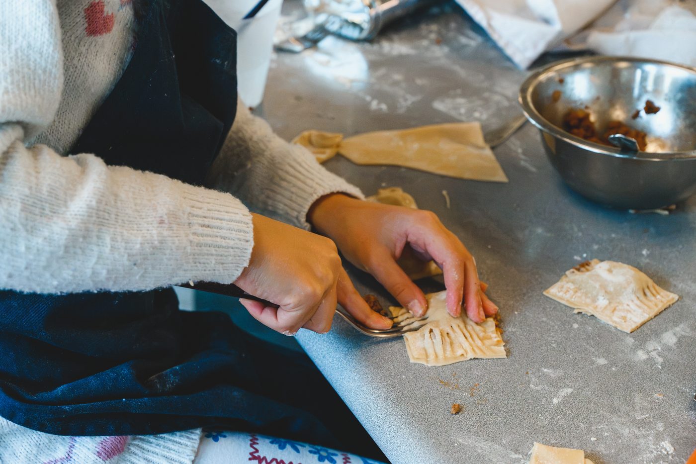 Hands crimping a filled pastry turnover with a fork on a floured bench