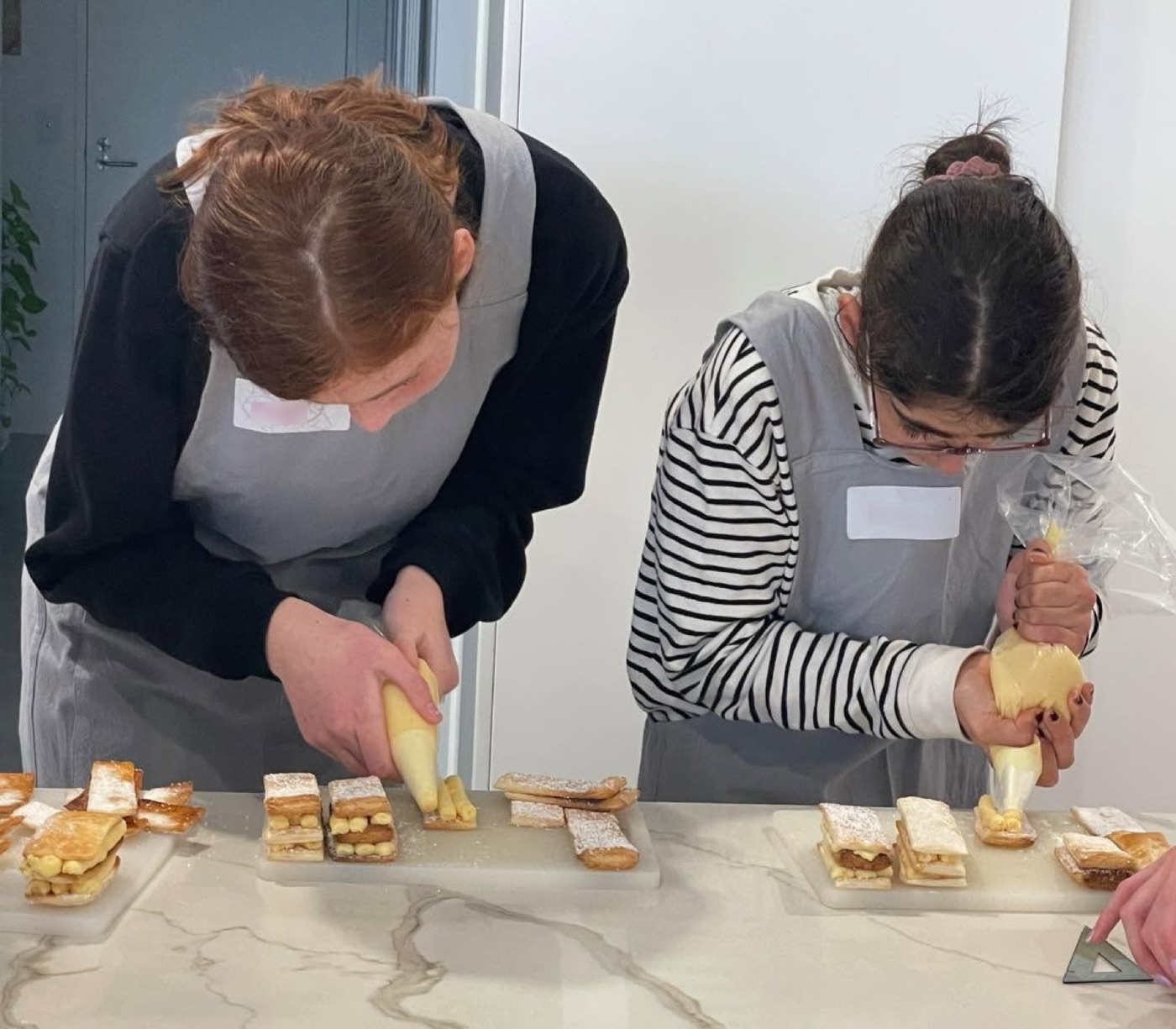 Two students piping cream onto pastry slices in a hands-on class
