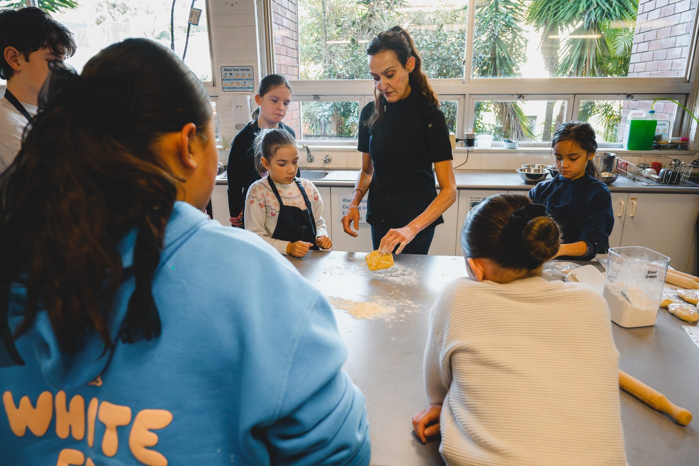 Yvonne shaping a piece of dough on the bench while five children watch closely.