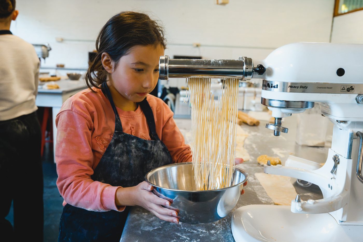 A girl holding a bowl to catch fresh spaghetti as it comes out of the pasta cutter.