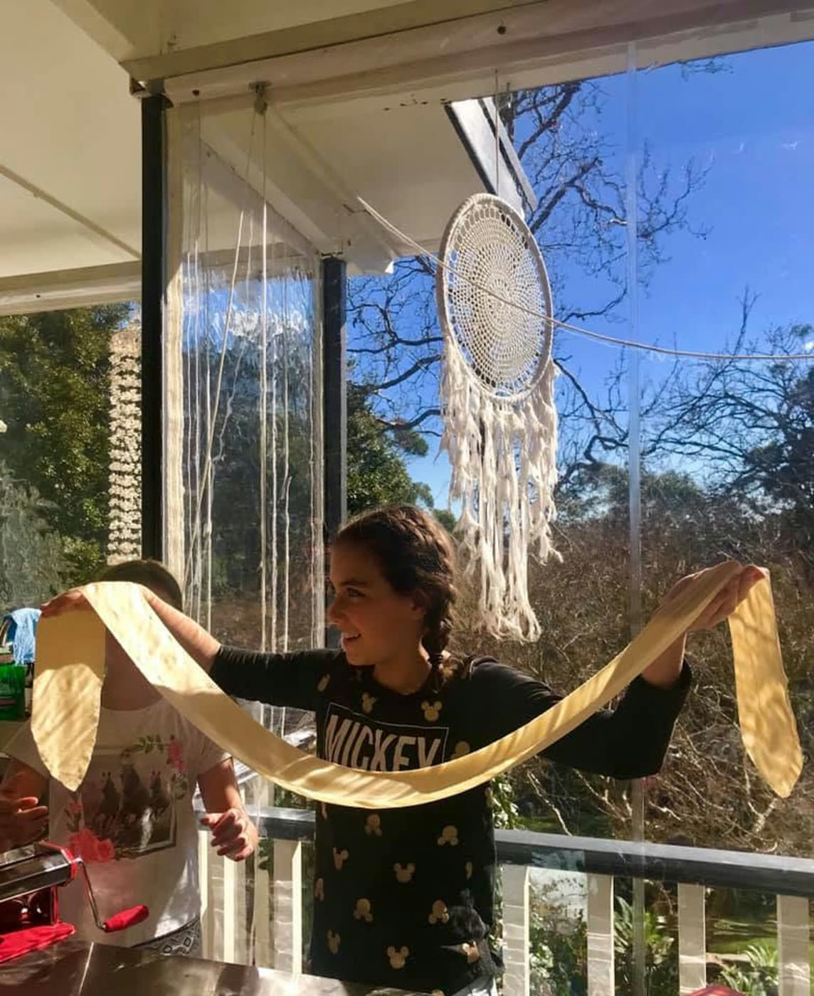 A girl on the deck holding up a long sheet of fresh pasta at arm span