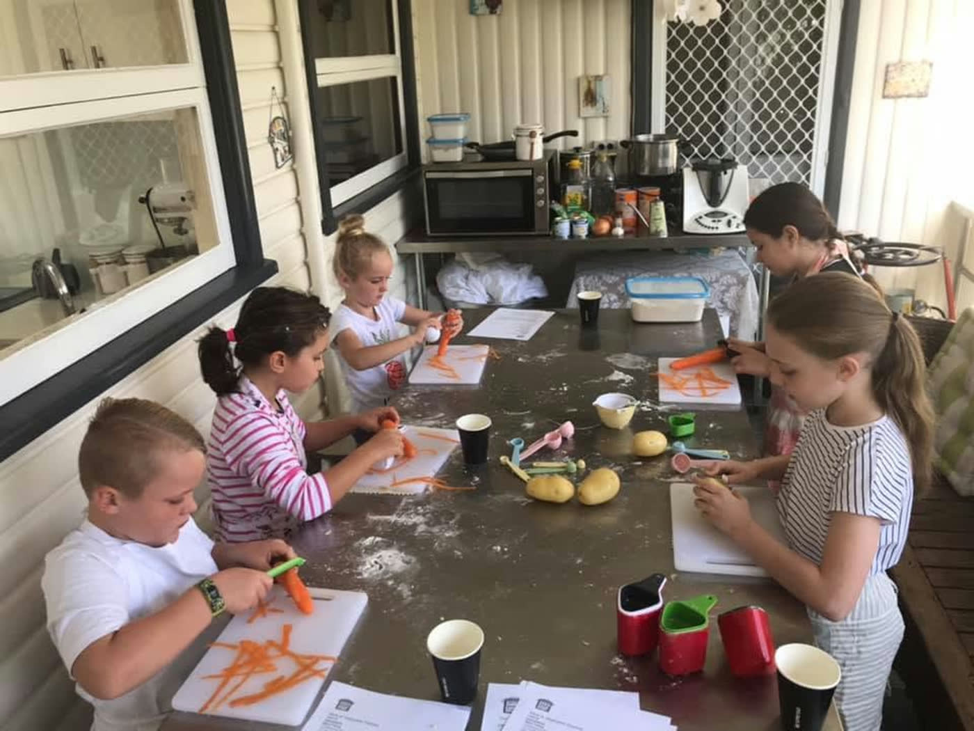 Children chopping carrots and vegetables along a long bench